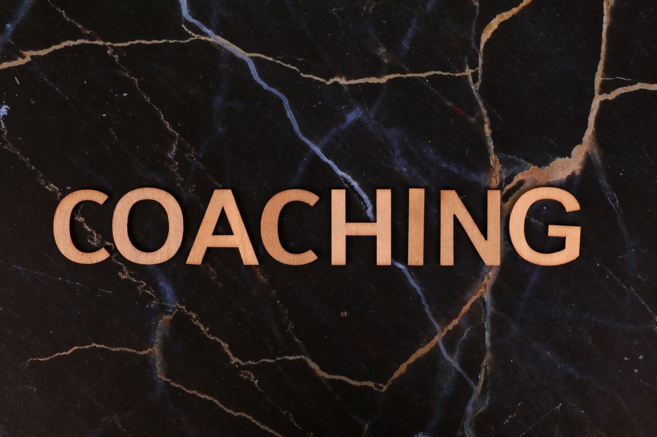 Wooden letters spelling 'Coaching' on dark marble surface, emphasizing guidance and mentorship.